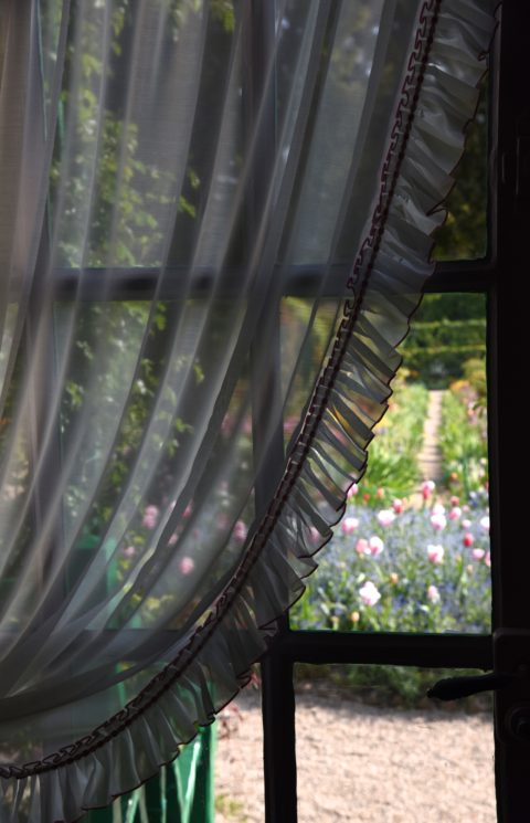 Window curtain and view of garden, travel inspiration at Monet's Giverny gardens. (Image © Meredith Mullins.)