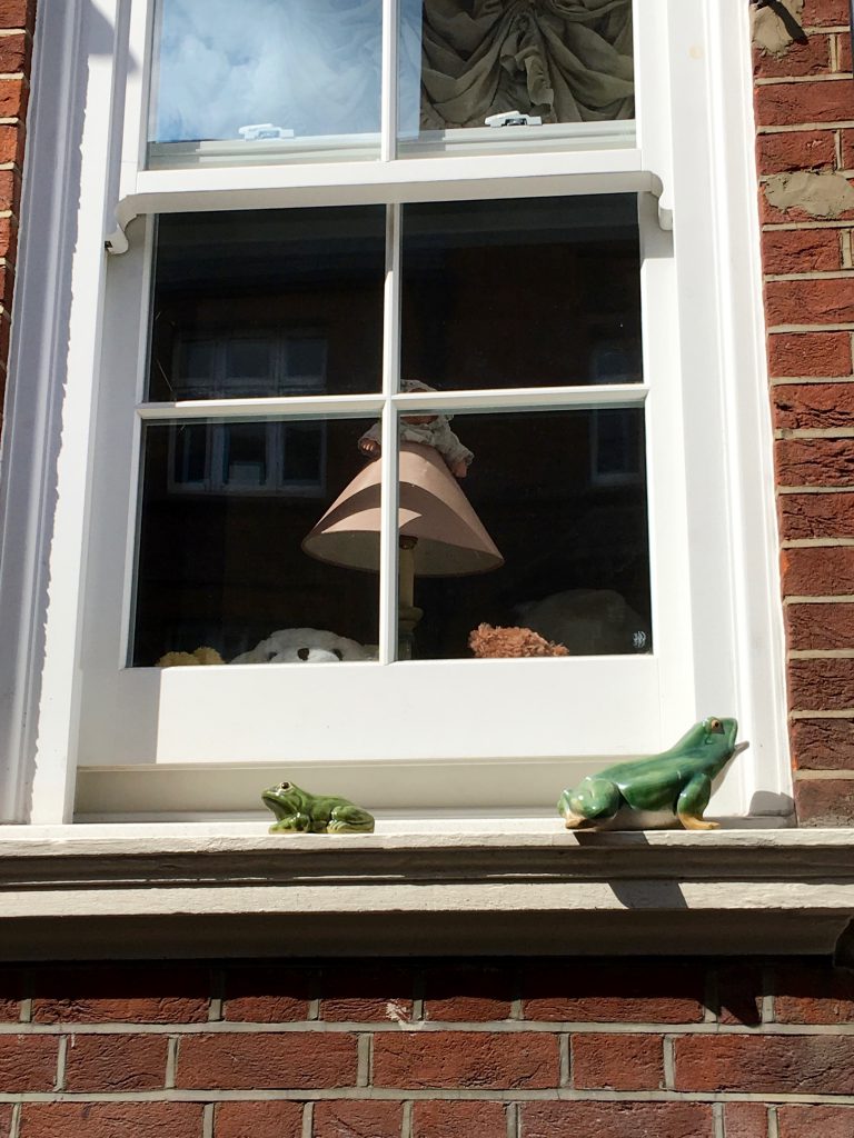 An English windowsill with two ceramic frogs on it, both delightful London details that are a travel inspiration. showcases whimsical London in close-up. (Image © Joyce McGreevy)