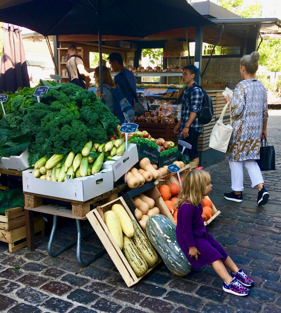 A little girl with Halloween pumpkins at a produce market in Copenhagen, Denmark exemplifies an aha moment about Halloween around the world. (Image © by Joyce McGreevy)