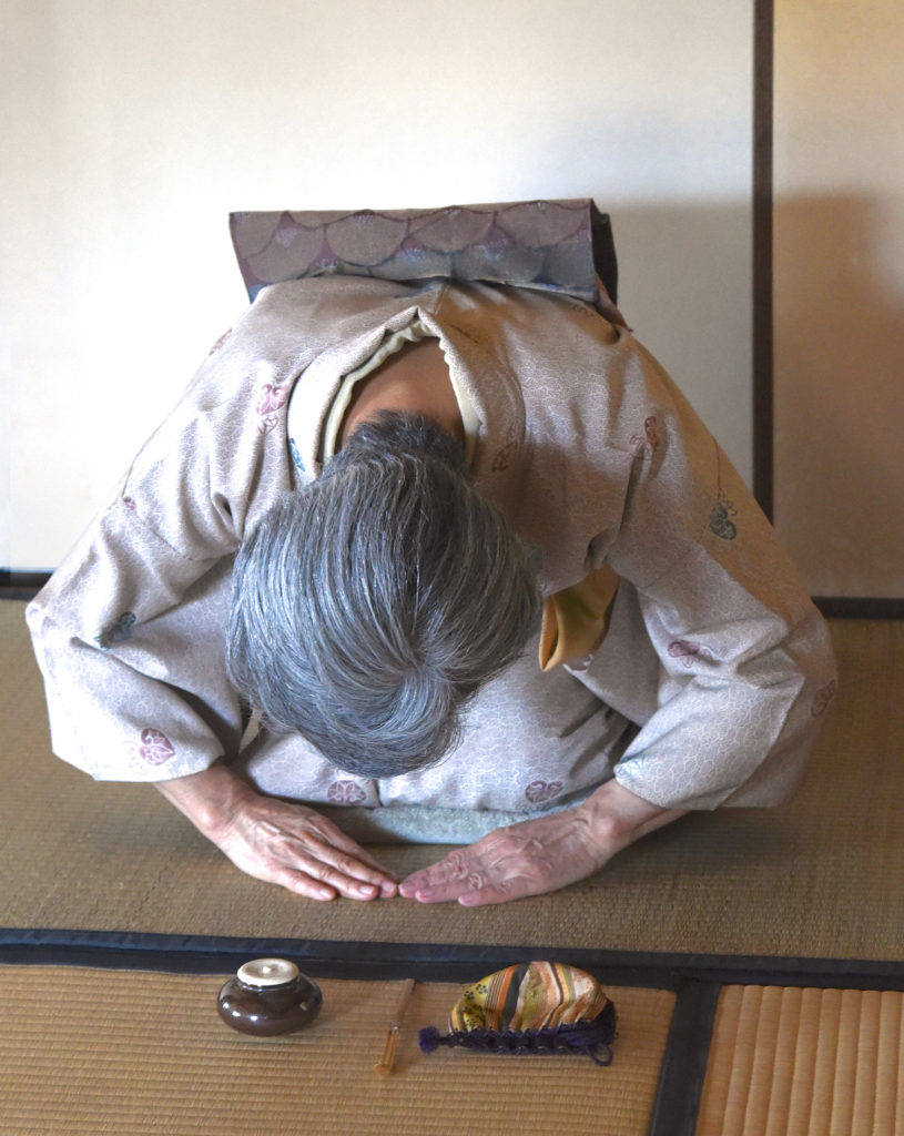 Japanese woman bows in front of utensils for the Japanese tea ceremony, showing the cultural traditions of Japan. (Image © Meredith Mullins.)