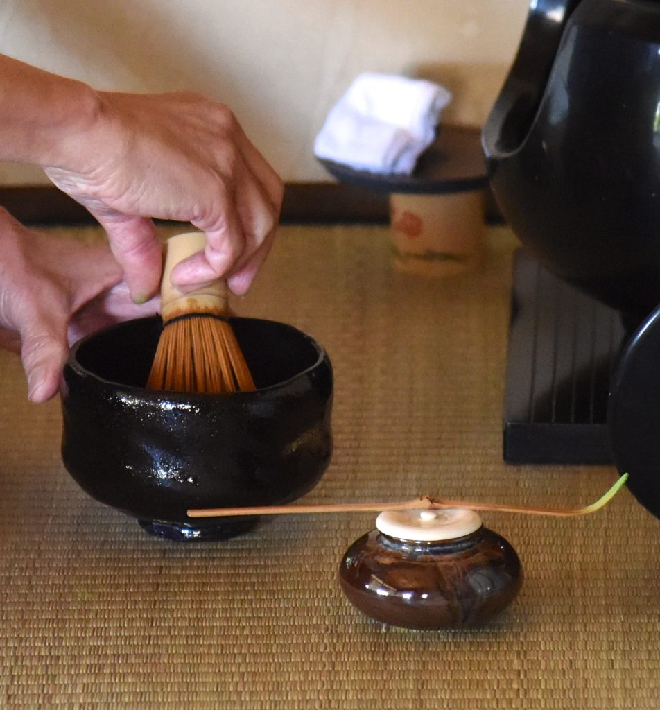 Hands whisking matcha tea in a bowl during the Japanese tea ceremony, showing the cultural traditions of Japan. (Image © Meredith Mullins.)