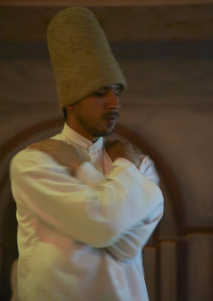 One of several whirling dervishes with arms crossed before beginning to dance in the Sufi Sema ceremony in Istanbul. (Image © Meredith Mullins)