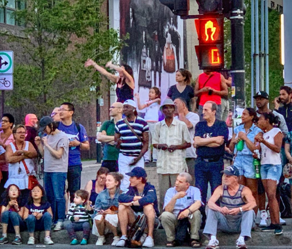 People gathered for a parade reminds the writer that each of us carries where we came from with us and all of us are traveling through life together. (Image © Joyce McGreevy)
