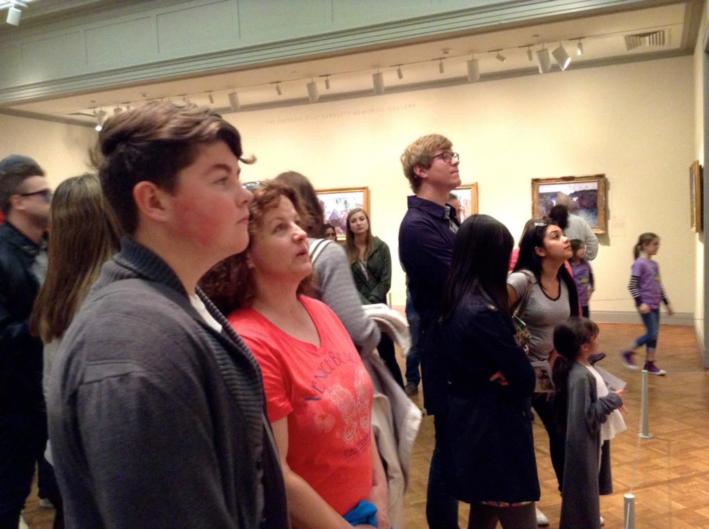 People looking at a painting at the Art Institute of Chicago exemplify the travel tip “slow down and focus.” (Image © by Joyce McGreevy)
