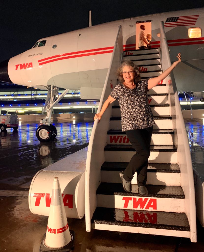 Carolyn McGreevy stands beside a TWA Constellation, or “Connie,” an airplane at the TWA Hotel at JFK Airport that evokes travel memories of Trans World Airlines. (Image © Joyce McGreevy)
