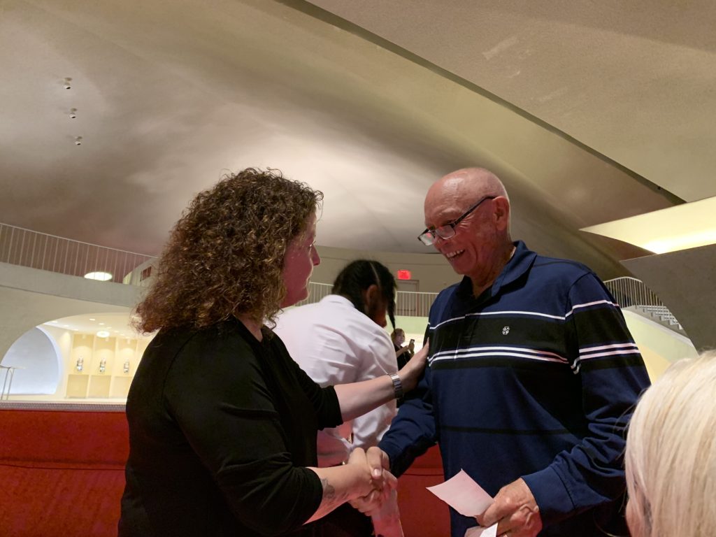 Trans World Airlines pilot’s daughter Margie McGreevy Cozad meets former TWA pilot Derwin “Dee” Grimm at the TWA Reunion, TWA Hotel, JFK Airport New York, where they share airline travel memories. (Image © Joyce McGreevy)