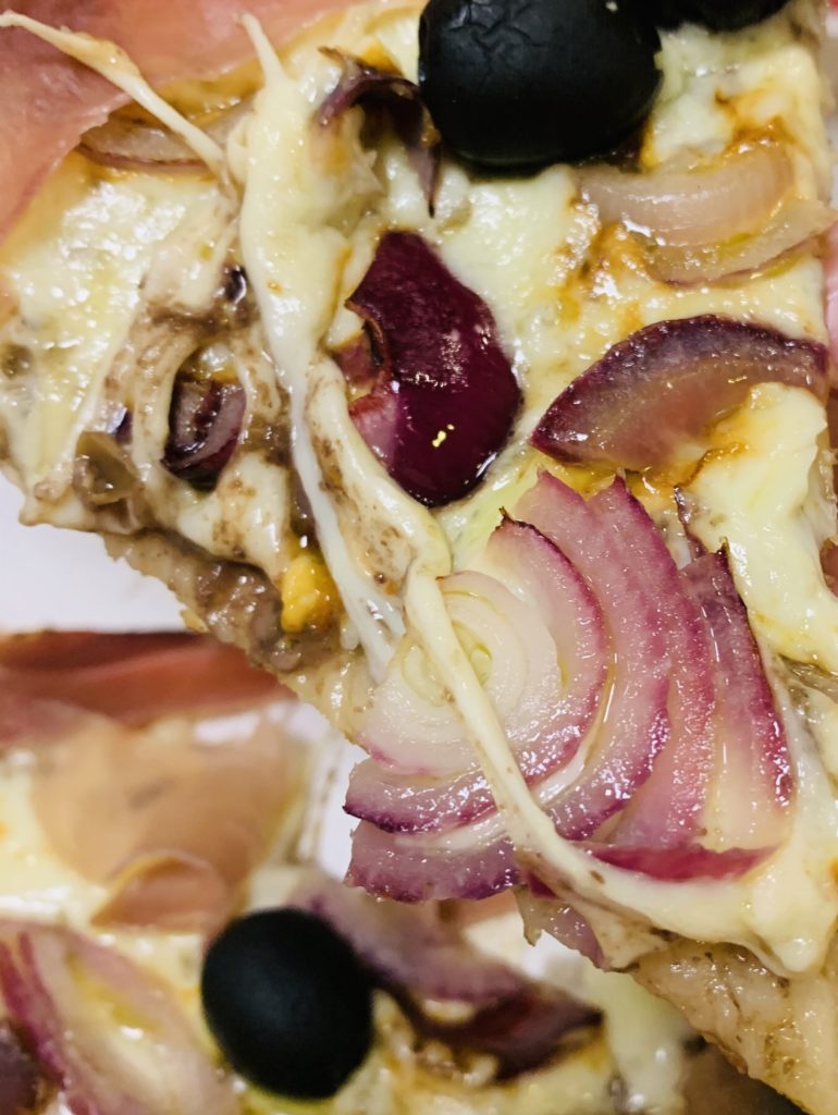 An onion-topped slice of Italian pizza shows why onions are a staple of global cuisine, crossing cultures from Italy to India. (Image © Joyce McGreevy)