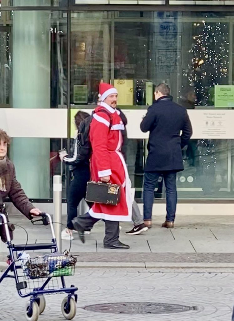 A man dressed as Father Christmas, spotted among pedestrians in Leipzig, Germany reflects the fun and whimsy of German Christmas traditions. (Image © Joyce McGreevy) 