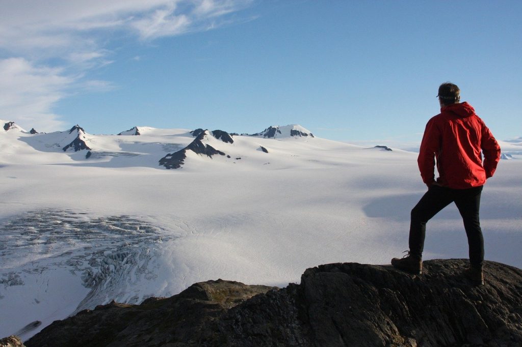 A mountain climber taking in the view from a peak reminds the author that 20/20 hindsight can actually be a valuable travel hack. (Public domain image by Skeeze/Pixabay)