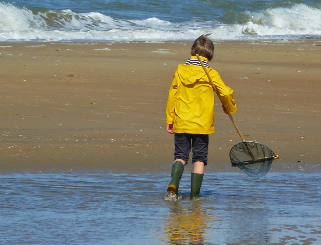 A boy at the beach wearing gum boots, wellies, or rain boots shows that English word meanings differ in different cultures, suggesting that crossing cultures is like learning a second language. (Public domain image by Pixabay)