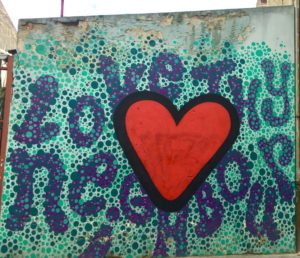 A mural of a heart on a city wall carries the proverb, “Love thy neighbor,” a cultural saying that is also an apt quarantine quote in the context of the Covid pandemic’s social distancing. (Image © Joyce McGreevy)