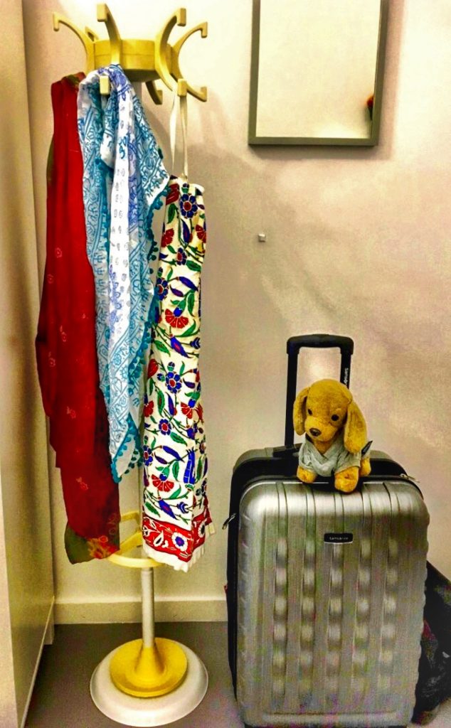 A coatrack, a suitcase, and a travel mascot in Greece remind a digital nomad of lessons learned from travel. (Image © by Joyce McGreevy)