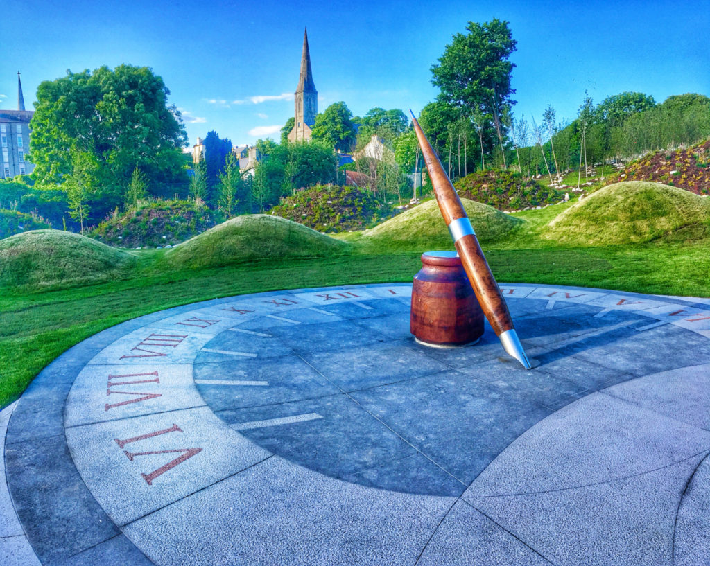A sun dial with a clock face and writing instruments in Ireland reminds a digital nomad of lessons learned from travel. (Image © by Joyce McGreevy