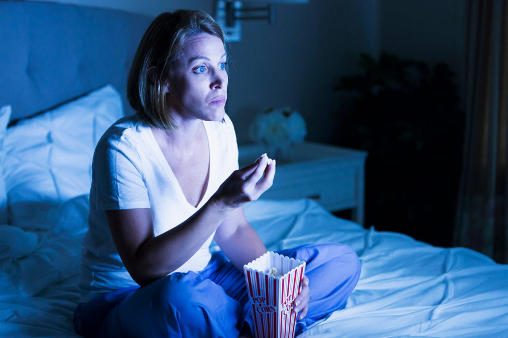 A woman binge-watching TV unknowingly embodies a language lesson—how you invent a word is influenced by other inventions, too. (Image by Kali9 and iStock)