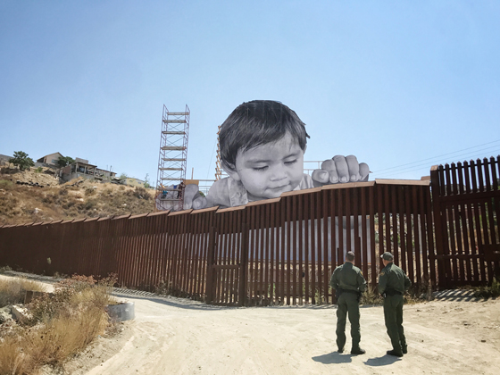 Artivist JR's pasting of a child looking over the USA Mexico border near Tecate Mexico, showing cultural diversity and social awareness and answering the question can art change the world. (Image © JR.)