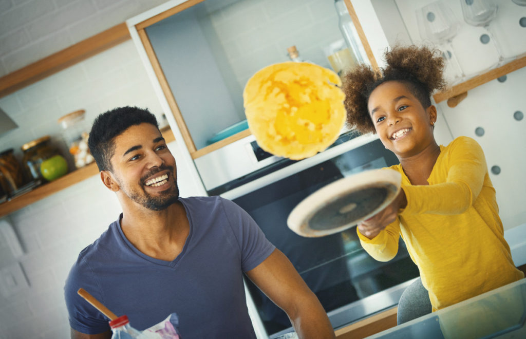 A father watching his daughter flip a pancake evokes the fun of cooking easy pancakes from around the world. (Image by Gilaxia and iStock)