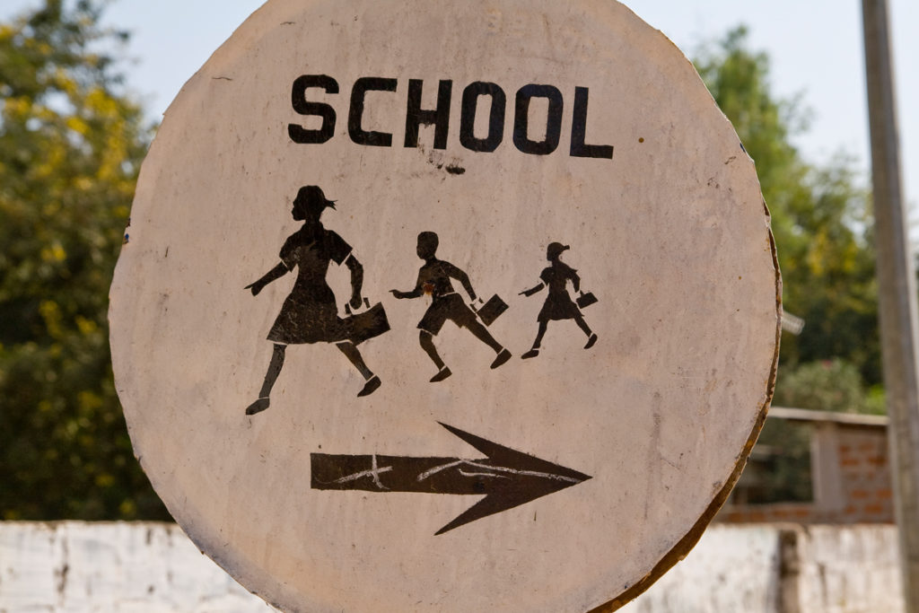 This round cardboard school zone sign from The Gambia with arrow pointing in one direction and 3 kids going in the opposite direction is part of a series of school zone signs from different cultures. Image © Kirszen/iStock 