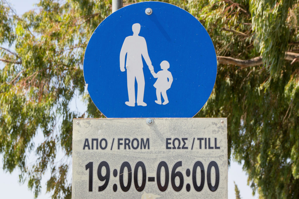 This blue circular school zone sign from Greece shows a father pulling his daughter along on her way to school and is part of a series of school zone signs from different cultures. Image © NeilLang/iStock.