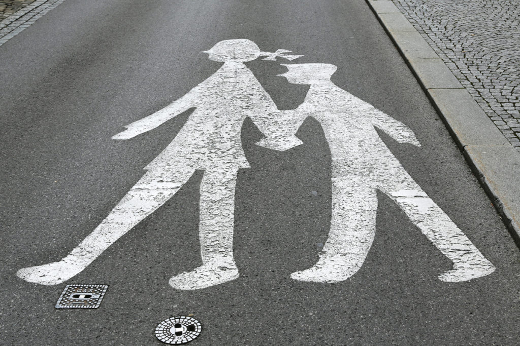 This school zone crosswalk features a girl with a bow in her pigtail guiding a boy with book in hand and is part of a series of school zone signs from different cultures. <br>Image © vikif/iStock.