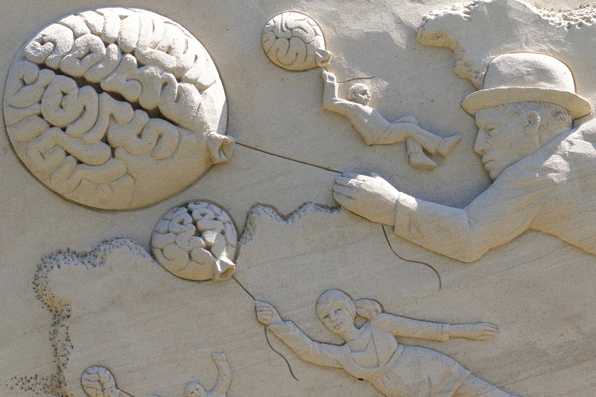 Sandstone sculpture of people holding balloons shaped like the human brain to illustrate how the bilingual brain lifts you up (Image © FotoEmotions/Pixabay))