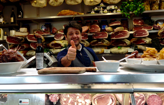 A view of an Italian merchant inside his deli and surrounded by salami to illustrate how wordplay around the world can be as slick as salami. 