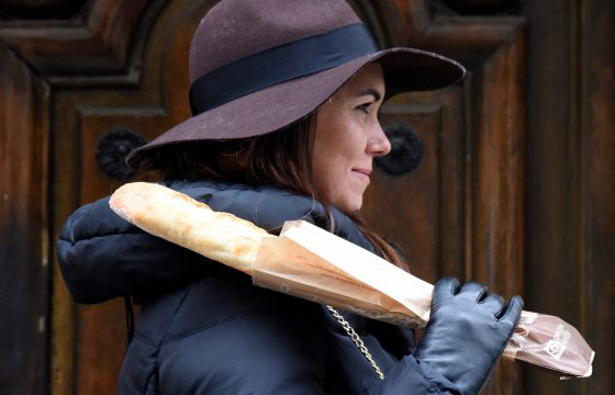 Young woman holding a baguette over her shoulder to illustrate an invented word "baguettetiquette" and lead to other invented words, which are a form of wordplay. (Image © Meredith Mullins).