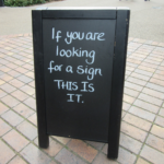 Chalkboard sign on sidewalk with the words "If you're looking for a sign, this is it", symbolizing the fun of wordplay across different cultures and languages. (Image © Matwor29/Pixabay)