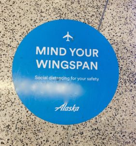 A floor marker at Alaska Airlines terminal in Los Angeles, as noted in an air traveler’s diary, reminds passengers to practice social distancing during the pandemic. (Image © Joyce McGreevy)