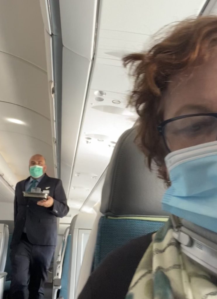 A flight attendant and a passenger keeping an air travel diary during the pandemic wear face masks to prevent the spread of the coronavirus. (Image © Joyce McGreevy)