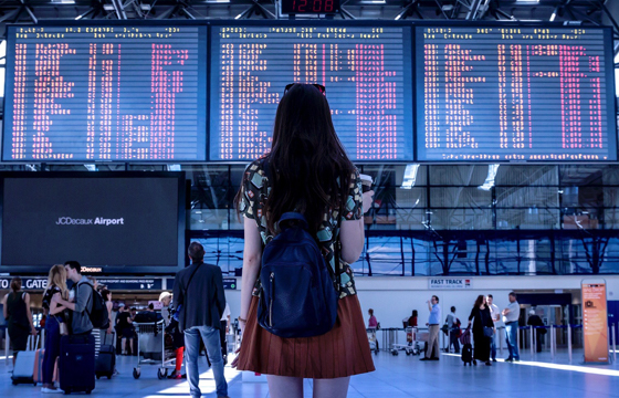 Young woman looking at an electronic board of airline departures to illustrate an interest in travel and building a bilingual brain (Image © Jan Vašek/Pixabay)