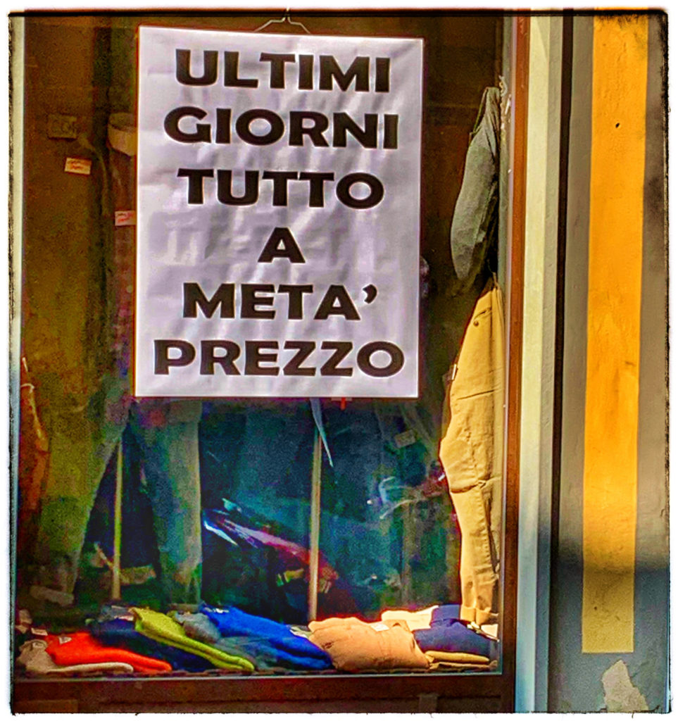 A sign in Italian advertising a half-price sale in Ferrara, illustrating why an important travel planning tip for Italy is to learn some Italian before you go. (Image © by Joyce McGreevy)